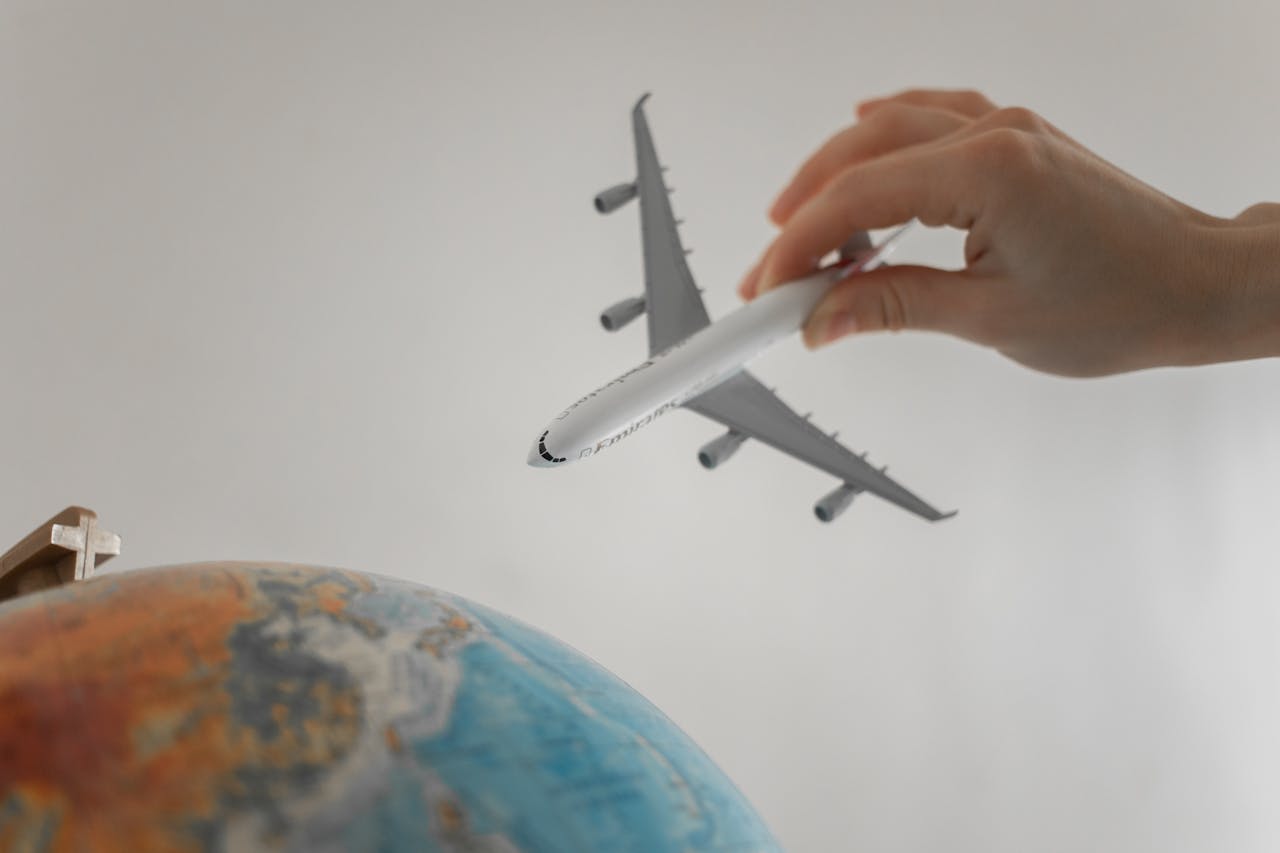 about-02 A hand holds a toy airplane above a globe, symbolizing travel and exploration.